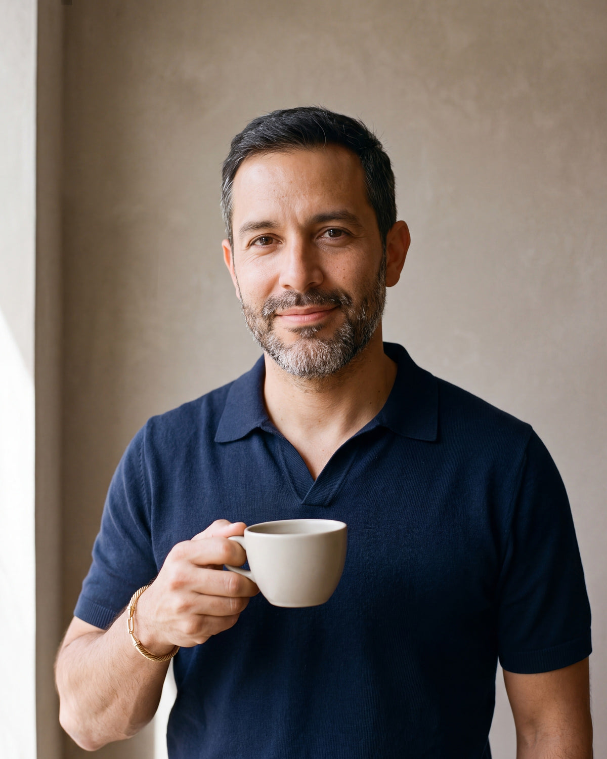 Man in a navy knit polo holding a coffee cup, wearing the gold-tone Atlas twisted cable bangle