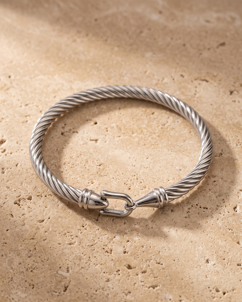 The silver Atlas twisted cable bangle on warm stone, horseshoe clasp