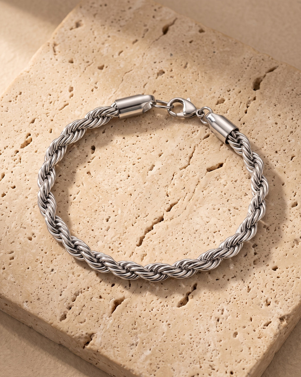 The whole silver-tone Atlas Twisted Rope Bracelet lying on warm travertine stone
