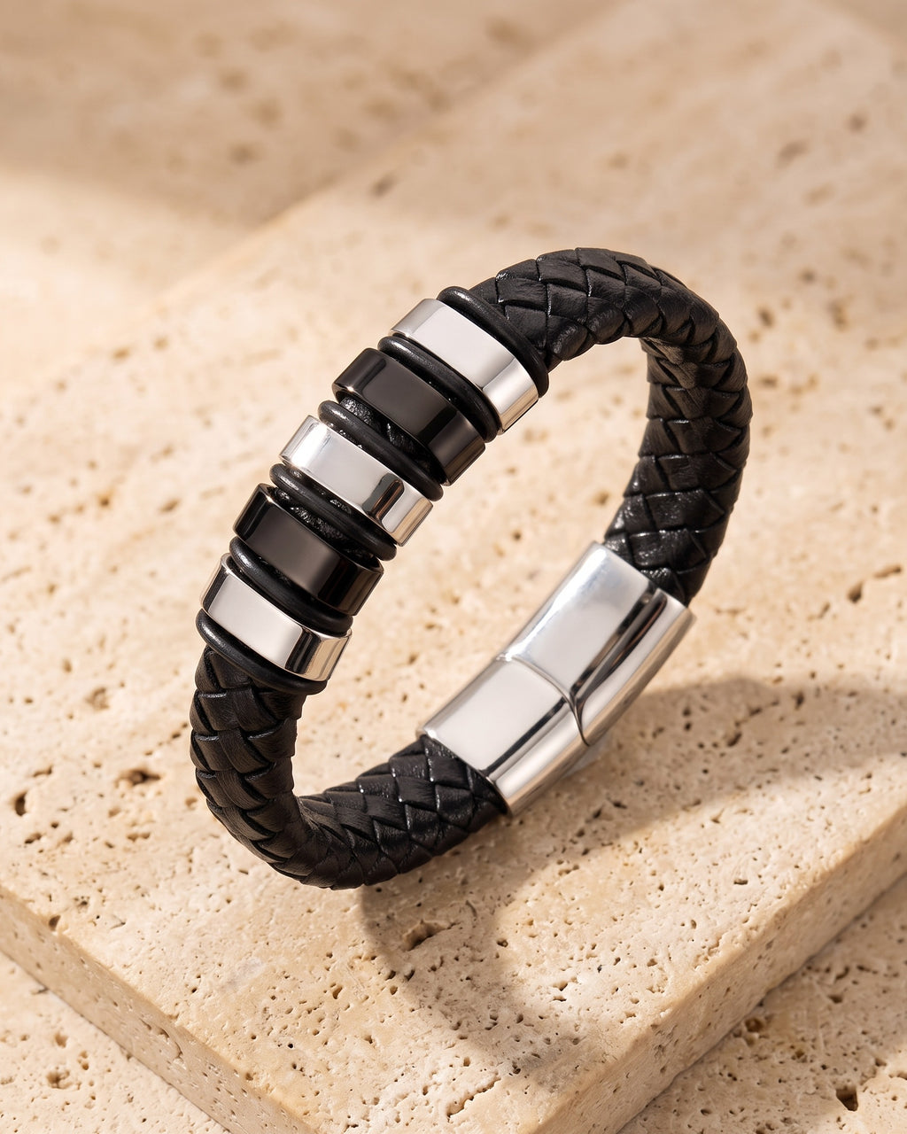 The whole silver-tone Atlas two-tone bar braided leather bracelet lying on warm travertine stone