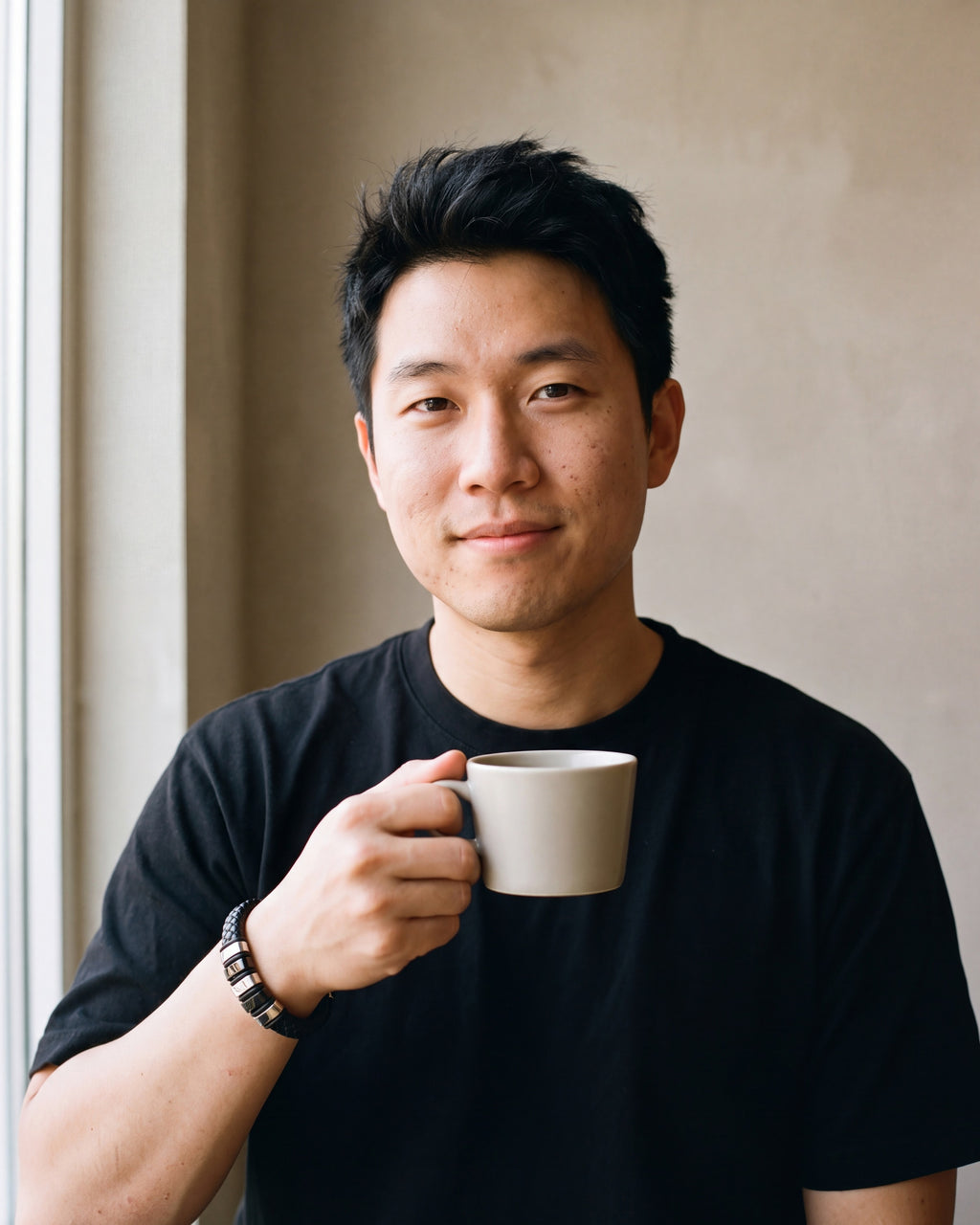 Man in a plain heavyweight black cotton crew-neck t-shirt (thick by a window wearing the silver-tone Atlas two-tone bar braided leather bracelet