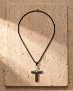 The black Atlas Two-Tone Cross Necklace with CZ laid on warm travertine stone