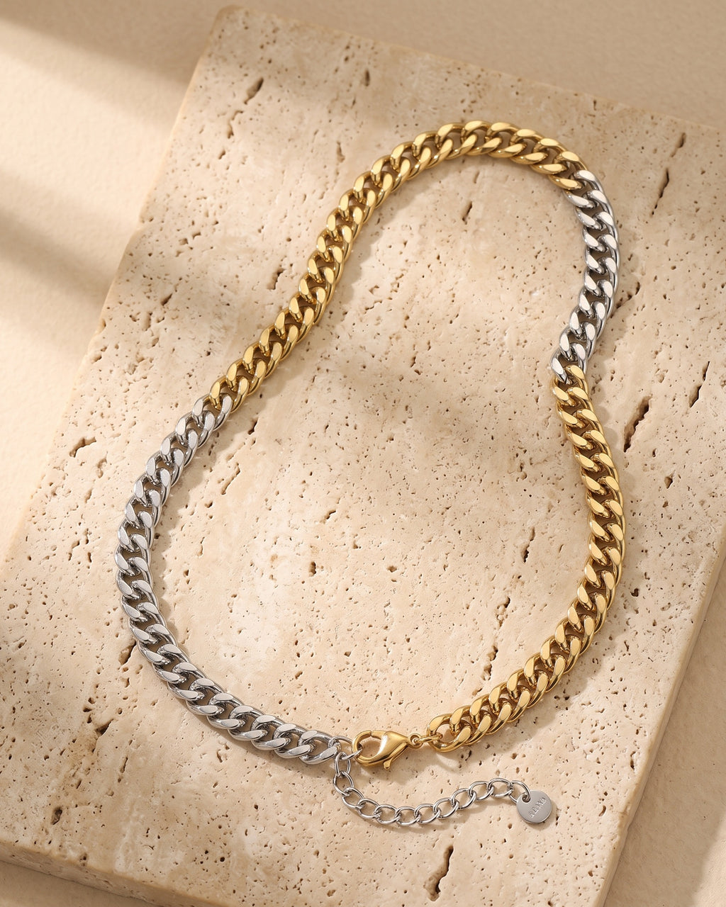 Atlas two-tone Cuban chain laid whole on warm stone, gold-tone and silver halves