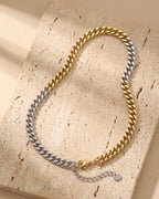 Atlas two-tone Cuban chain laid whole on warm stone, gold-tone and silver halves