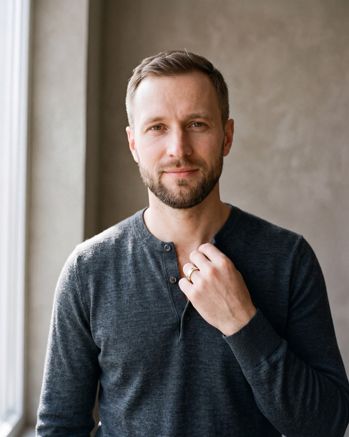Man in a fine-gauge charcoal-grey merino knit with a henley neckline by a window wearing the plain Atlas two-tone frosted band