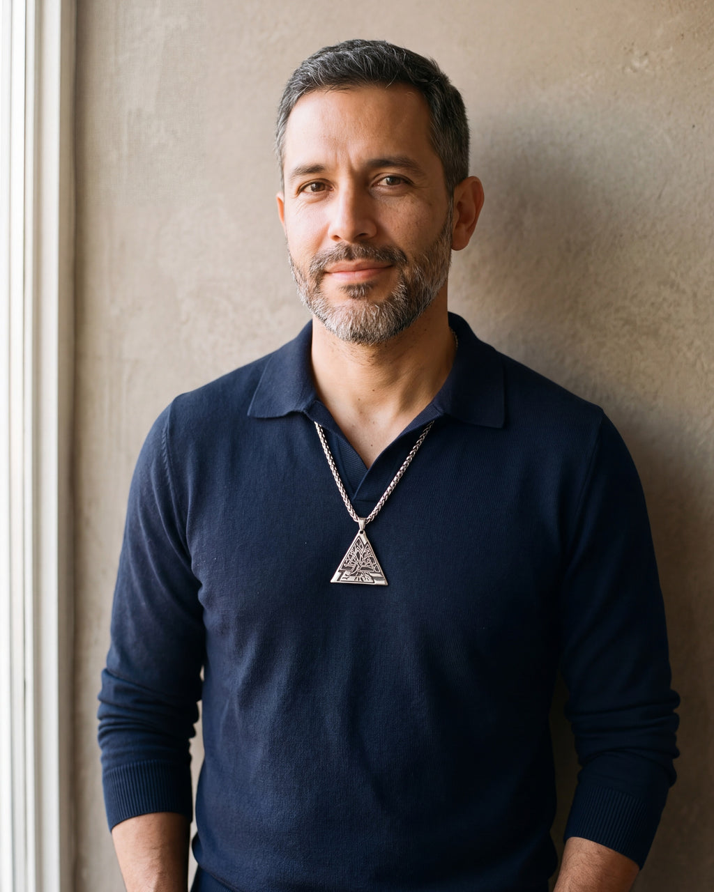 Man in a navy knit polo wearing the Atlas Valknut triangle pendant necklace
