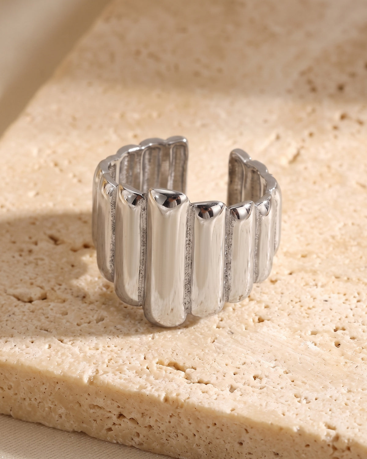 The whole silver Atlas vertical stripe cuff ring lying on warm travertine stone