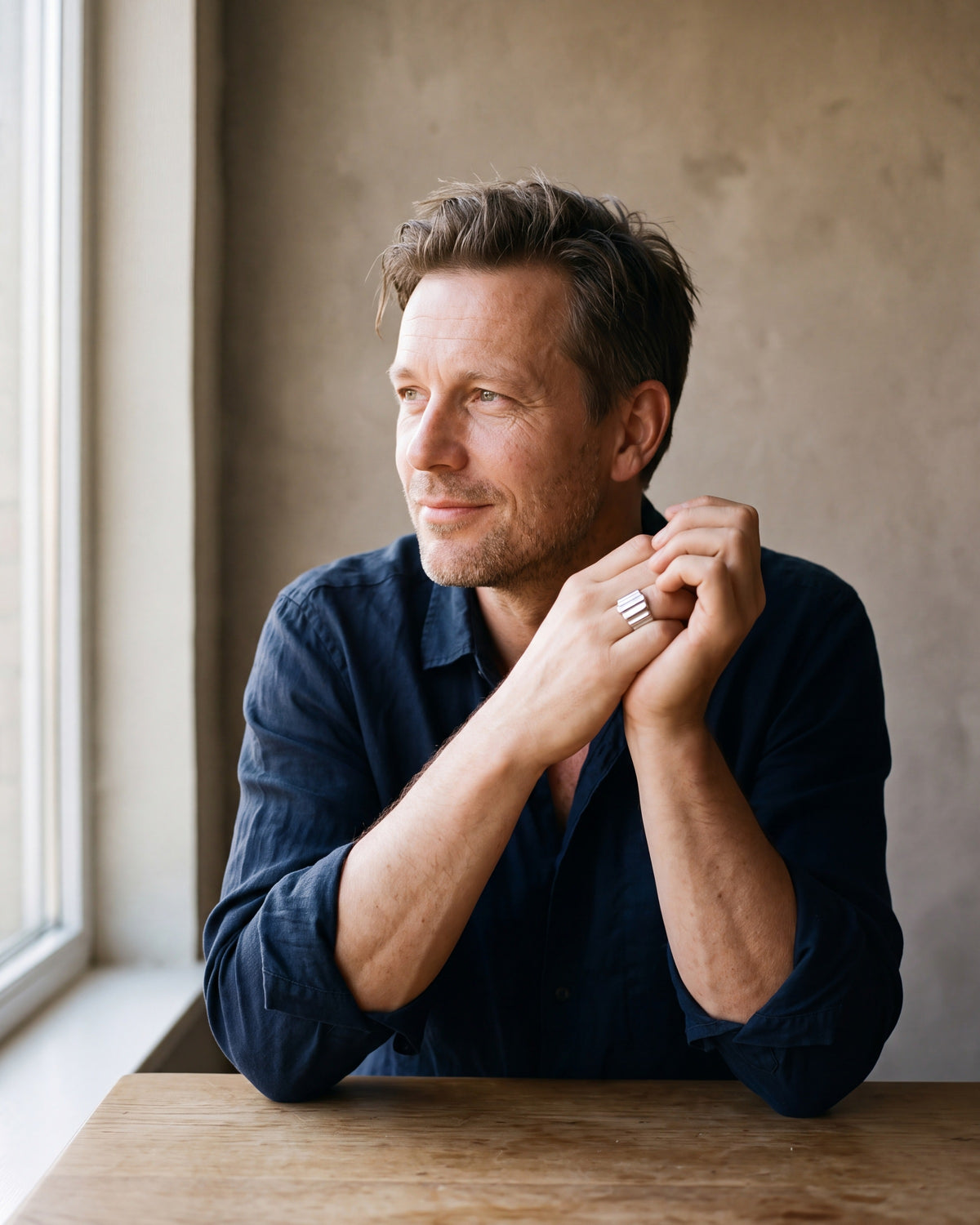 Man in a dark navy linen shirt by a window wearing the silver Atlas vertical stripe cuff ring