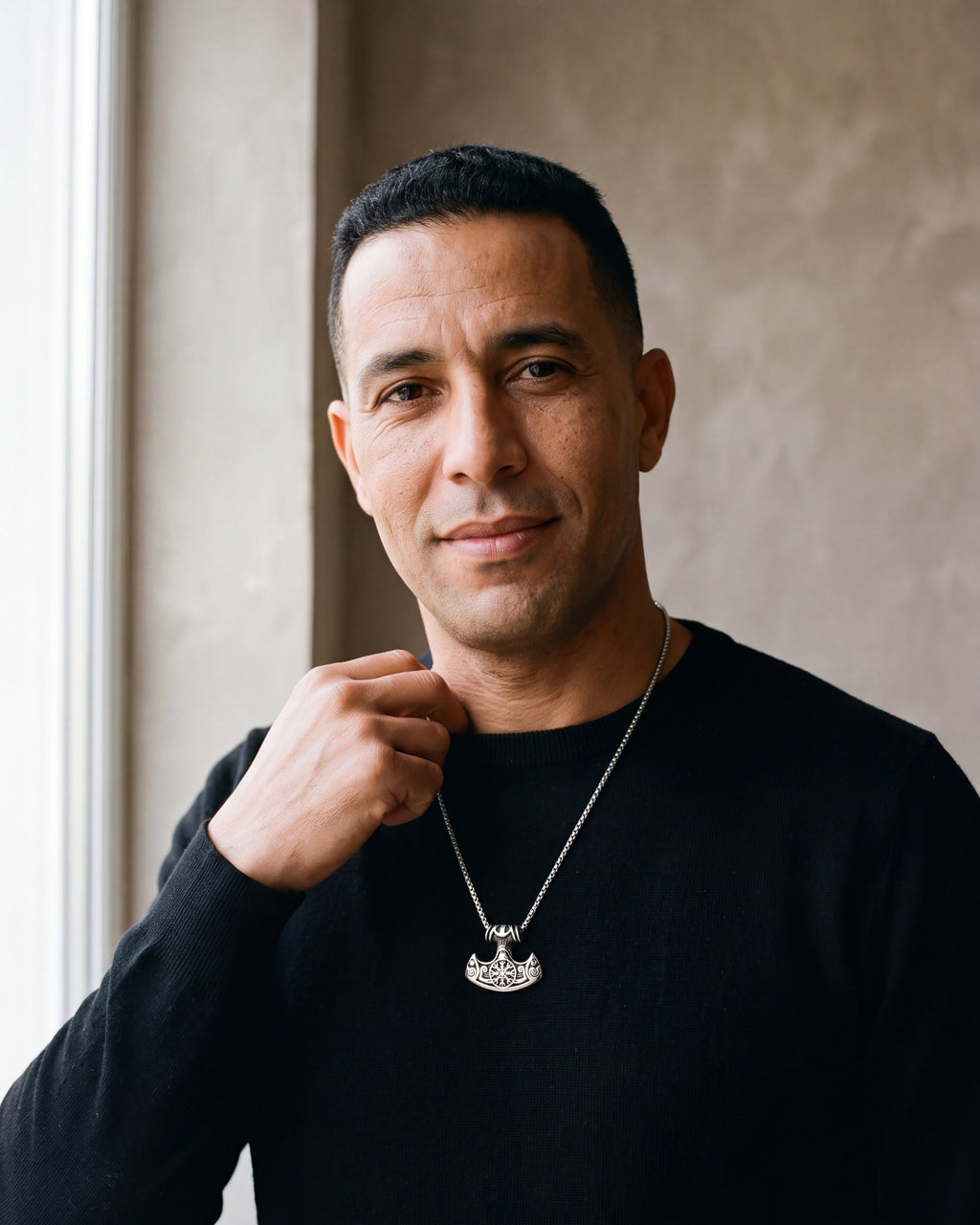 Man in a black merino crew-neck sweater by a window wearing the silver Atlas viking hammer pendant necklace