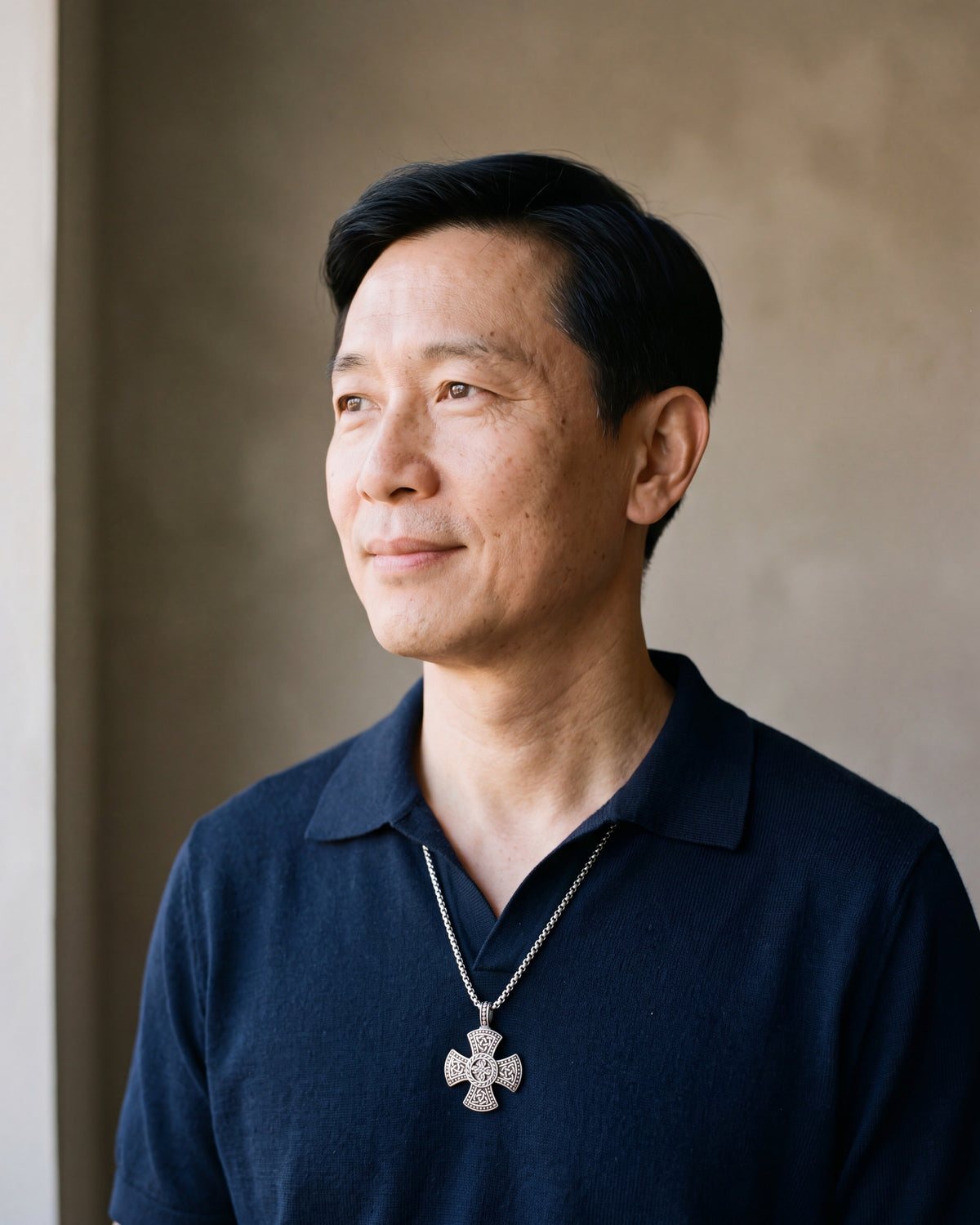 Man in a navy knit polo wearing the Atlas Viking knotwork cross pendant necklace in silver-tone steel