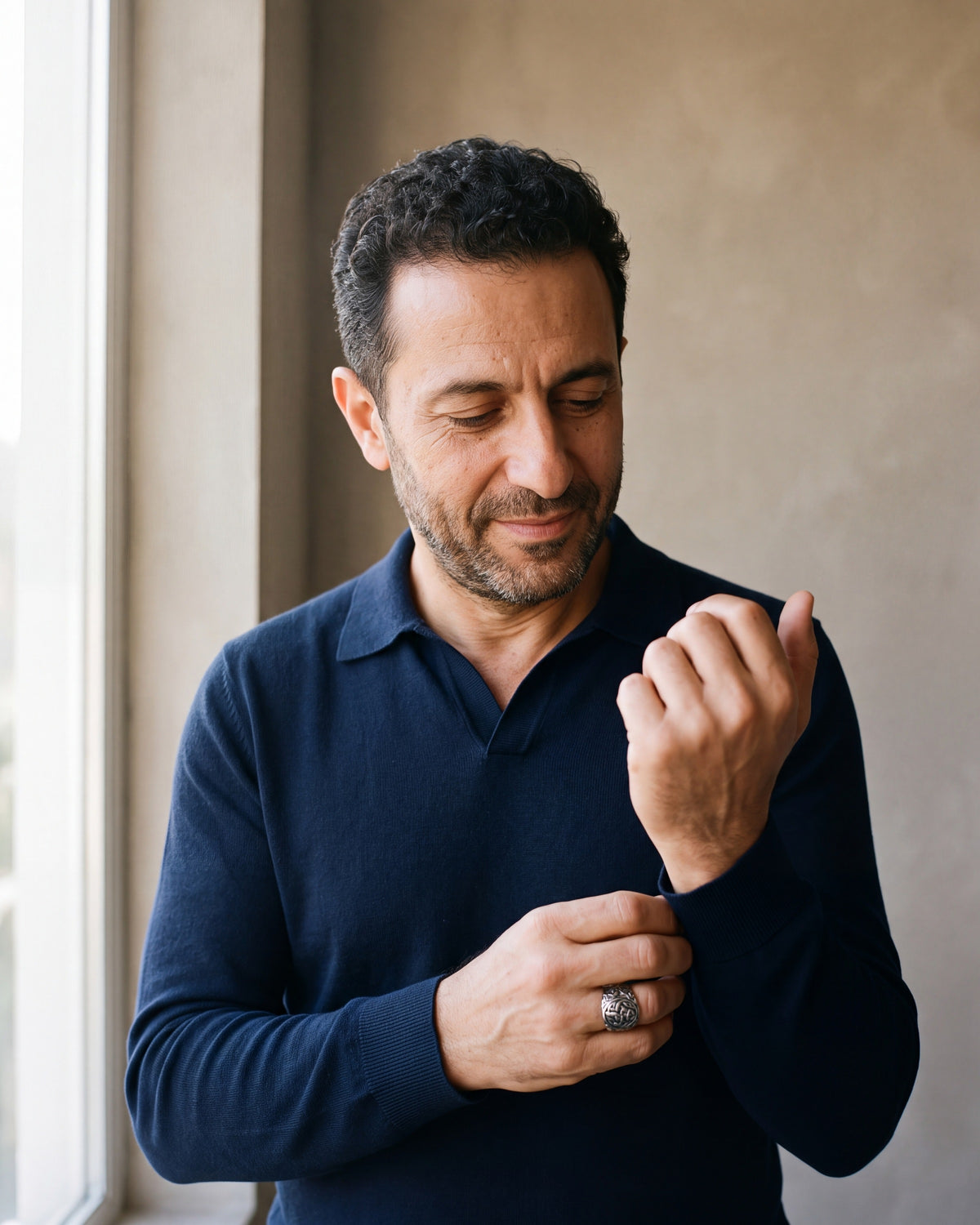 Man in a navy knit polo adjusting his sleeve wearing the antiqued silver-tone Atlas Viking knotwork ring