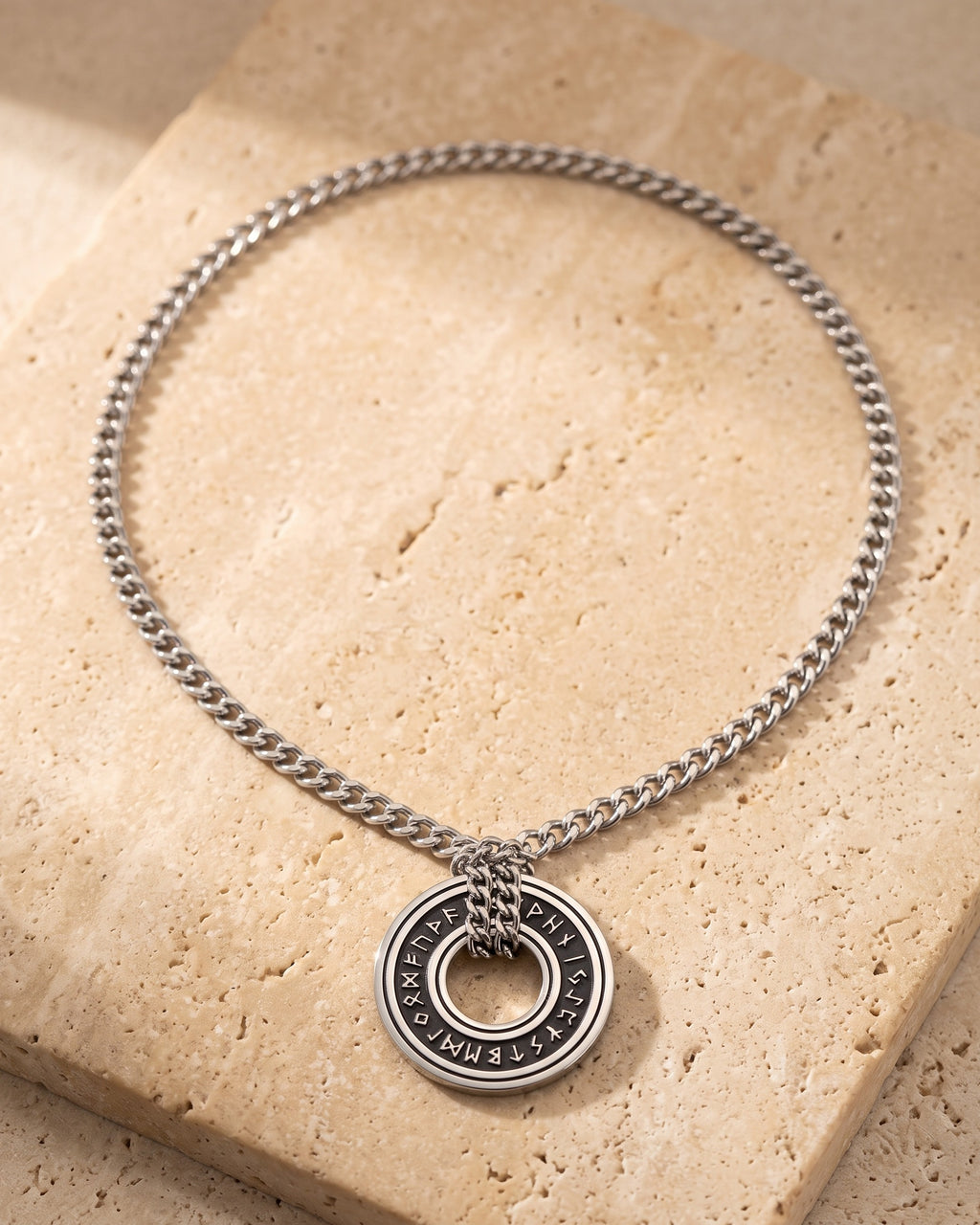 Entire Atlas Viking rune circle pendant necklace in silver-tone steel, lying flat on warm stone