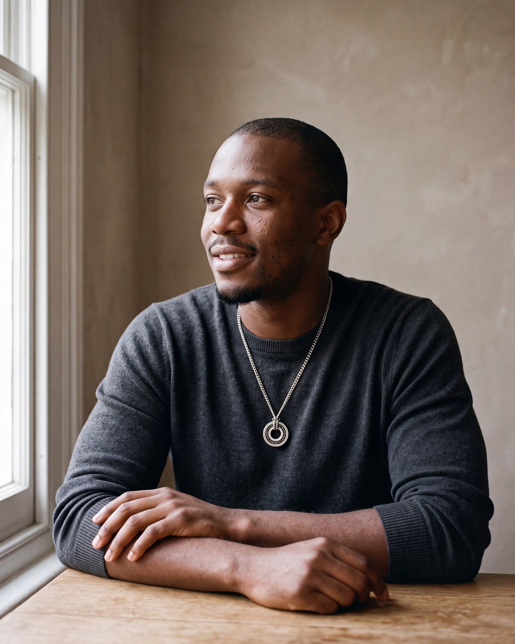 Man in a charcoal knit sweater by a window wearing the Atlas Viking rune circle pendant necklace in silver-tone steel