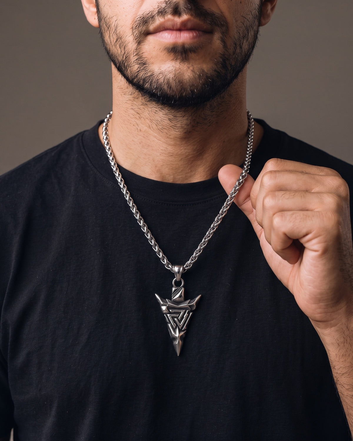 Hand lifting the Atlas Viking Valknut Arrow Necklace at the collarbone