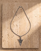 The silver Atlas Viking Valknut Arrow Necklace laid on warm travertine stone
