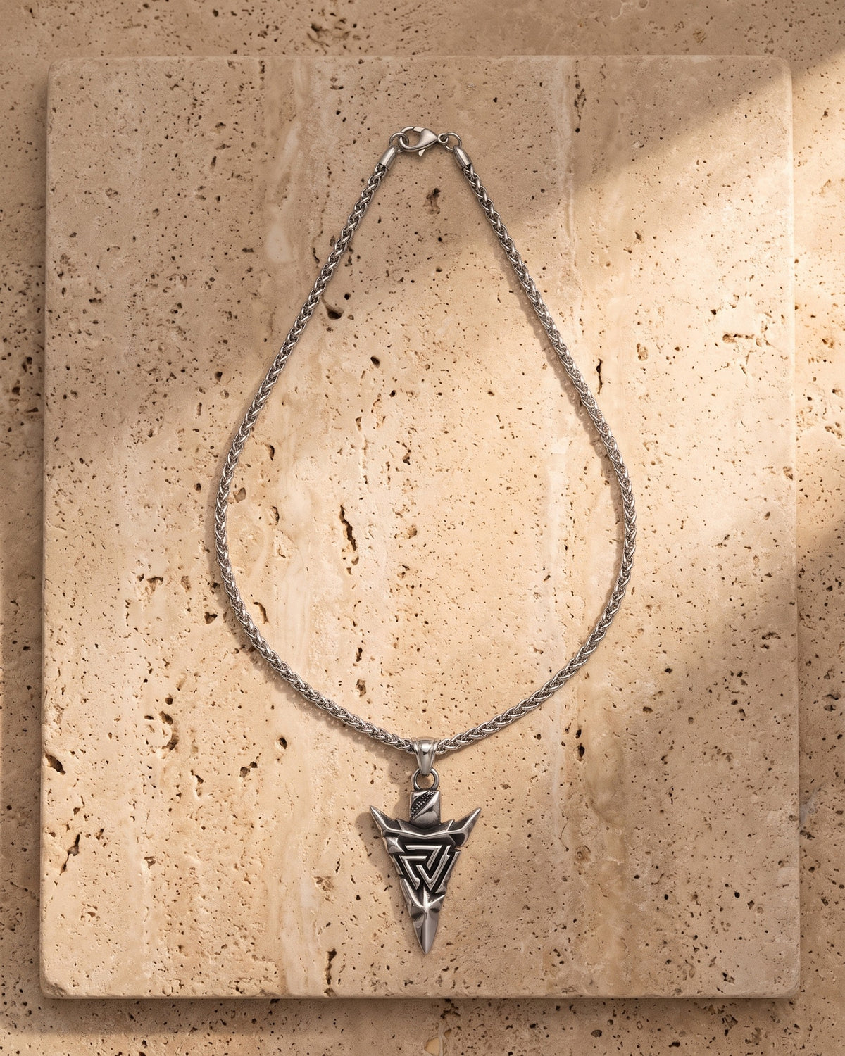 The silver Atlas Viking Valknut Arrow Necklace laid on warm travertine stone