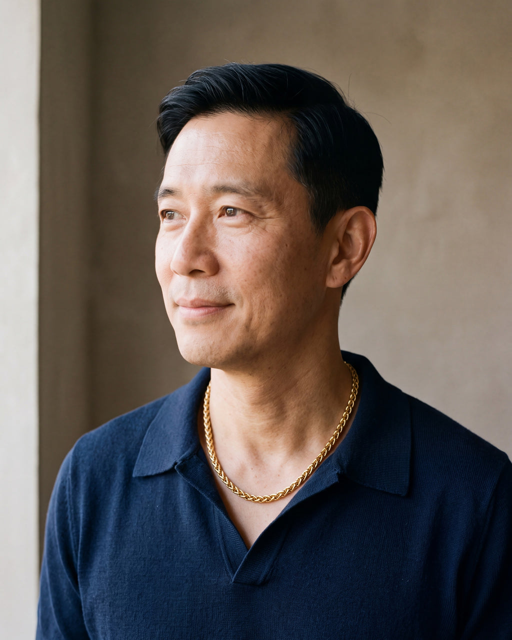 Man in a navy knit polo wearing the Atlas wheat chain in gold-tone steel