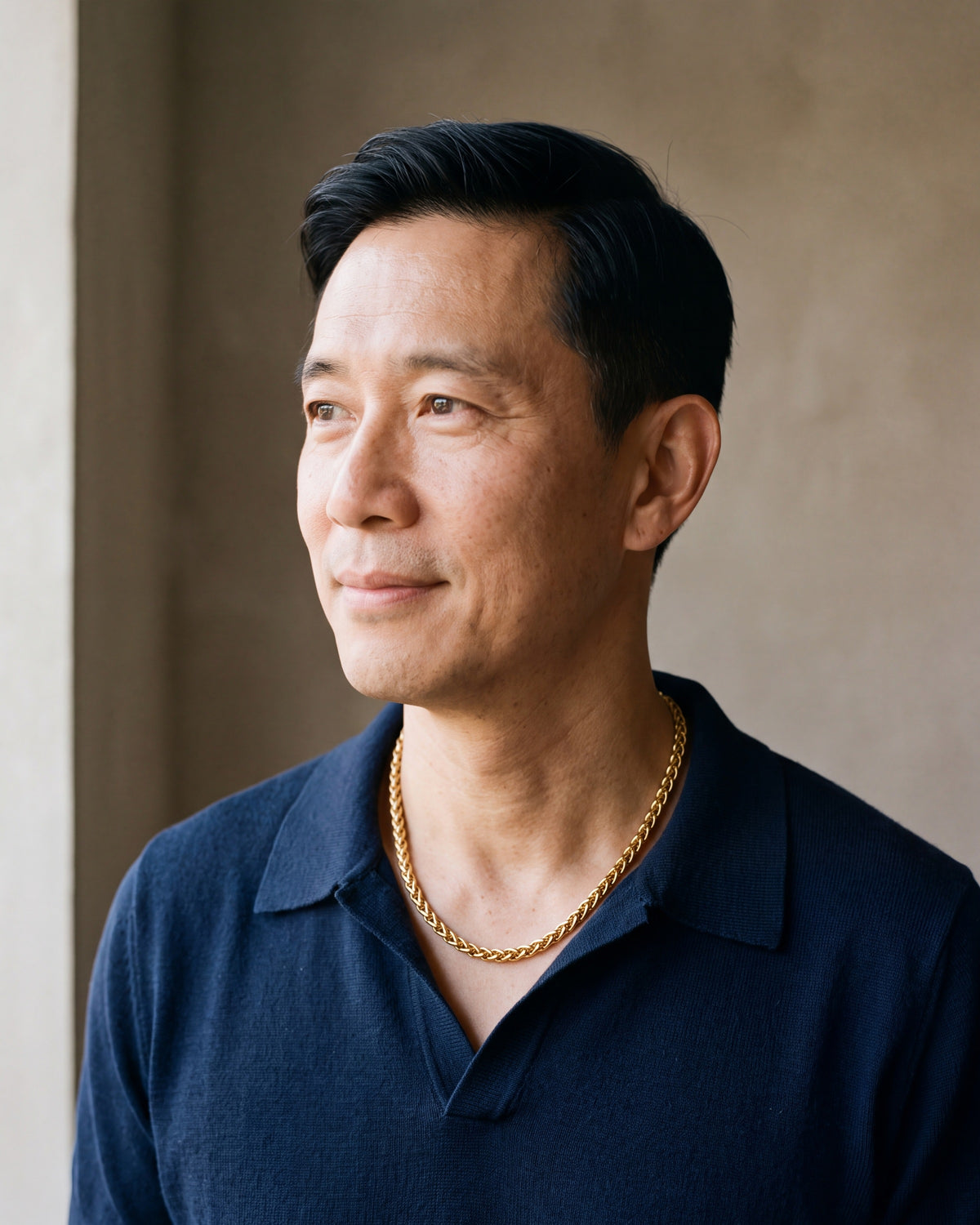 Man in a navy knit polo wearing the Atlas wheat chain in gold-tone steel