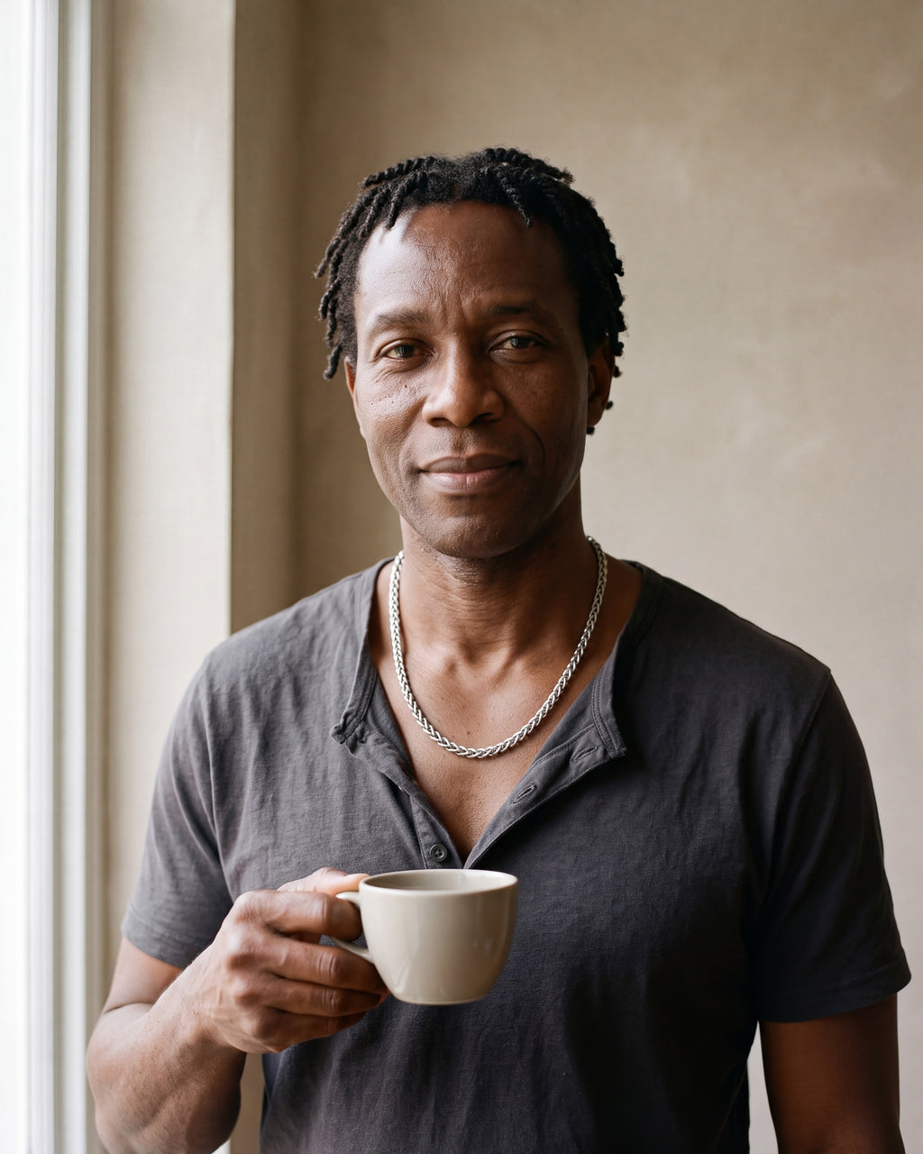 Man in a charcoal cotton henley t-shirt by a window wearing the silver Atlas wheat chain