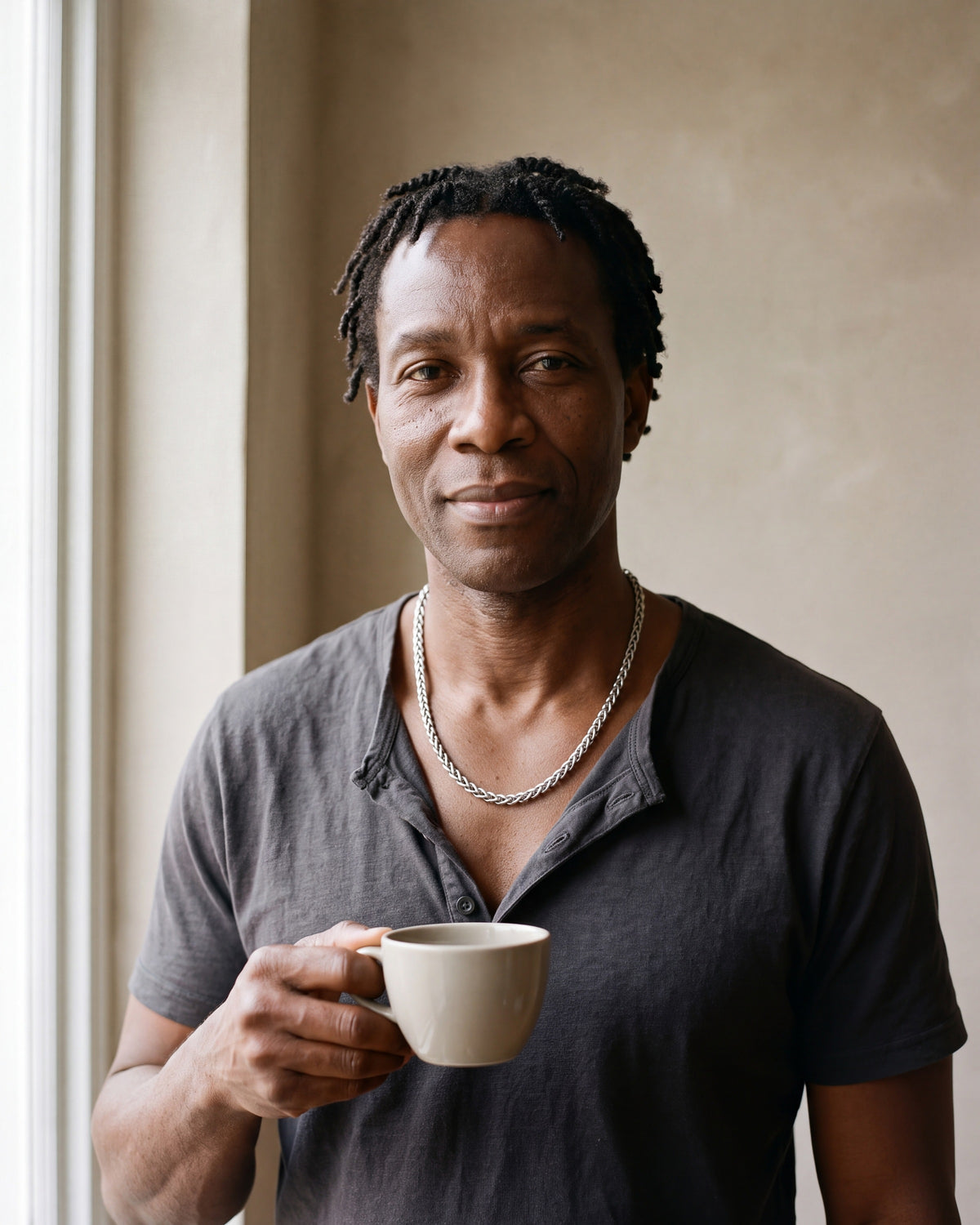 Man in a charcoal cotton henley t-shirt by a window wearing the silver Atlas wheat chain