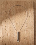 The silver Atlas Whistle Pendant Necklace in Titanium Steel laid on warm travertine stone