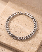 The silver Atlas Wide Cuban Link Bracelet in Titanium Steel laid on warm travertine stone