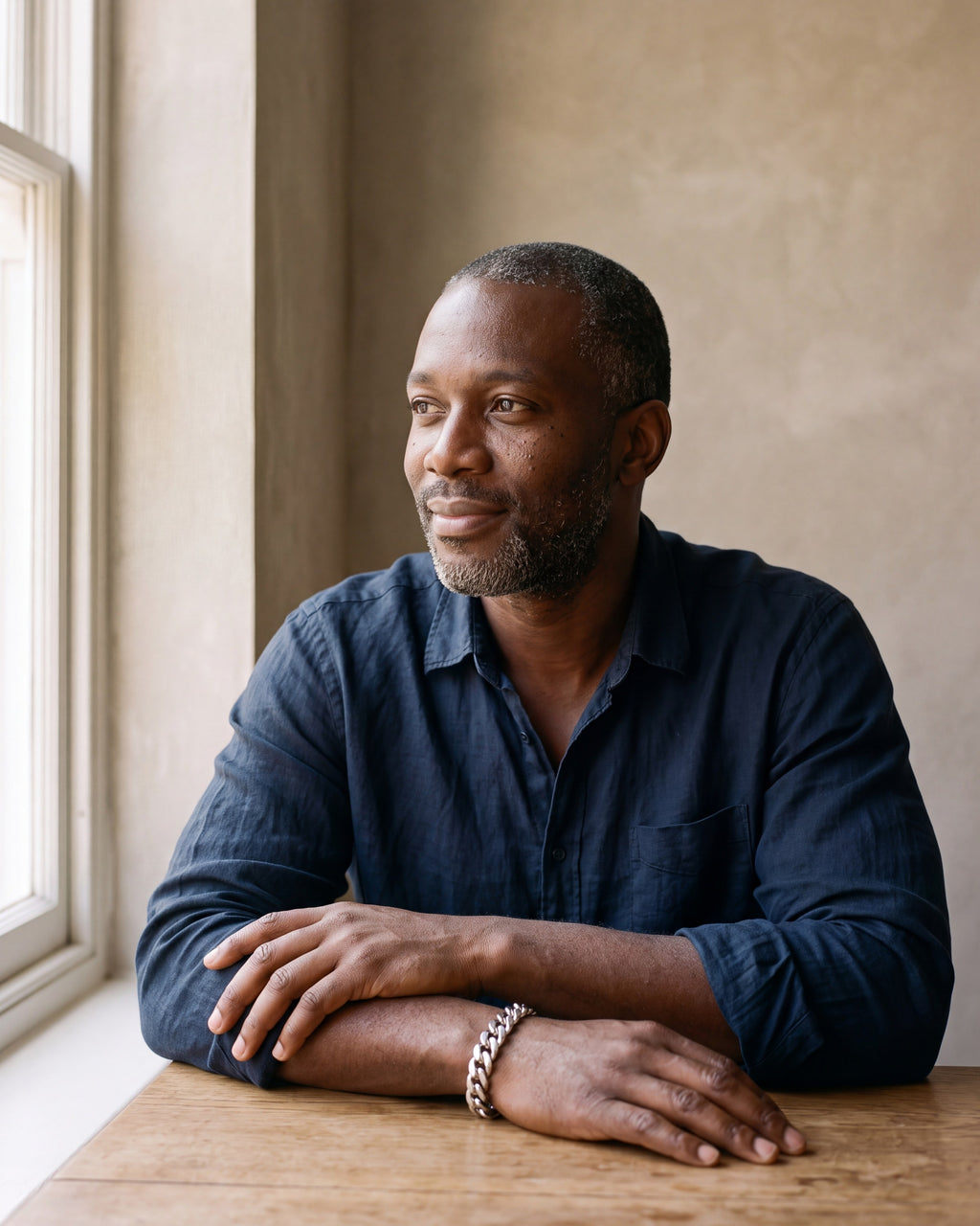 Man in a navy linen shirt seated at a wooden table wearing the silver Atlas wide Cuban link bracelet