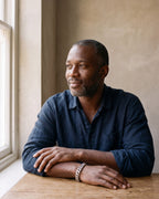 Man in a navy linen shirt seated at a wooden table wearing the silver Atlas wide Cuban link bracelet