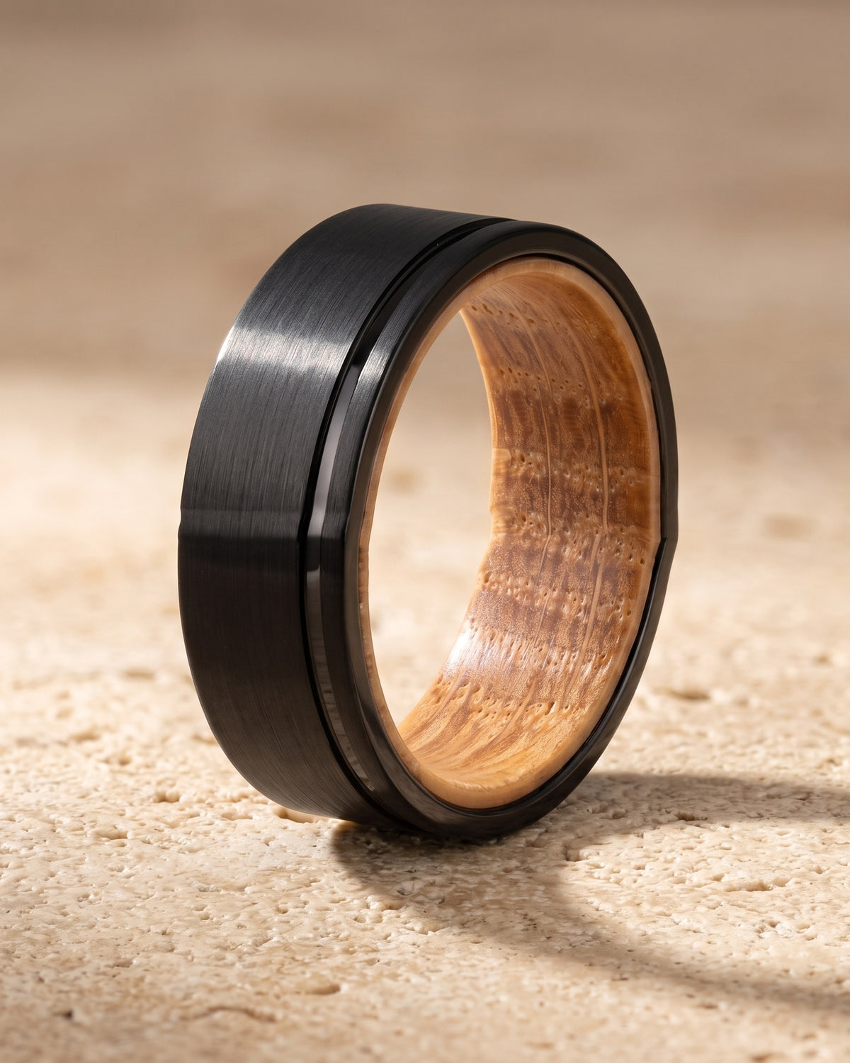 The whole black Atlas Wine Barrel Wood Ring lying on warm travertine stone