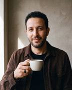 Man in a dark brown suede overshirt open over a black t-shirt by a window wearing the black Atlas Wine Barrel Wood Ring
