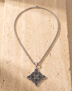 The whole silver-tone Atlas Celtic witch's knot pendant necklace lying on warm travertine stone