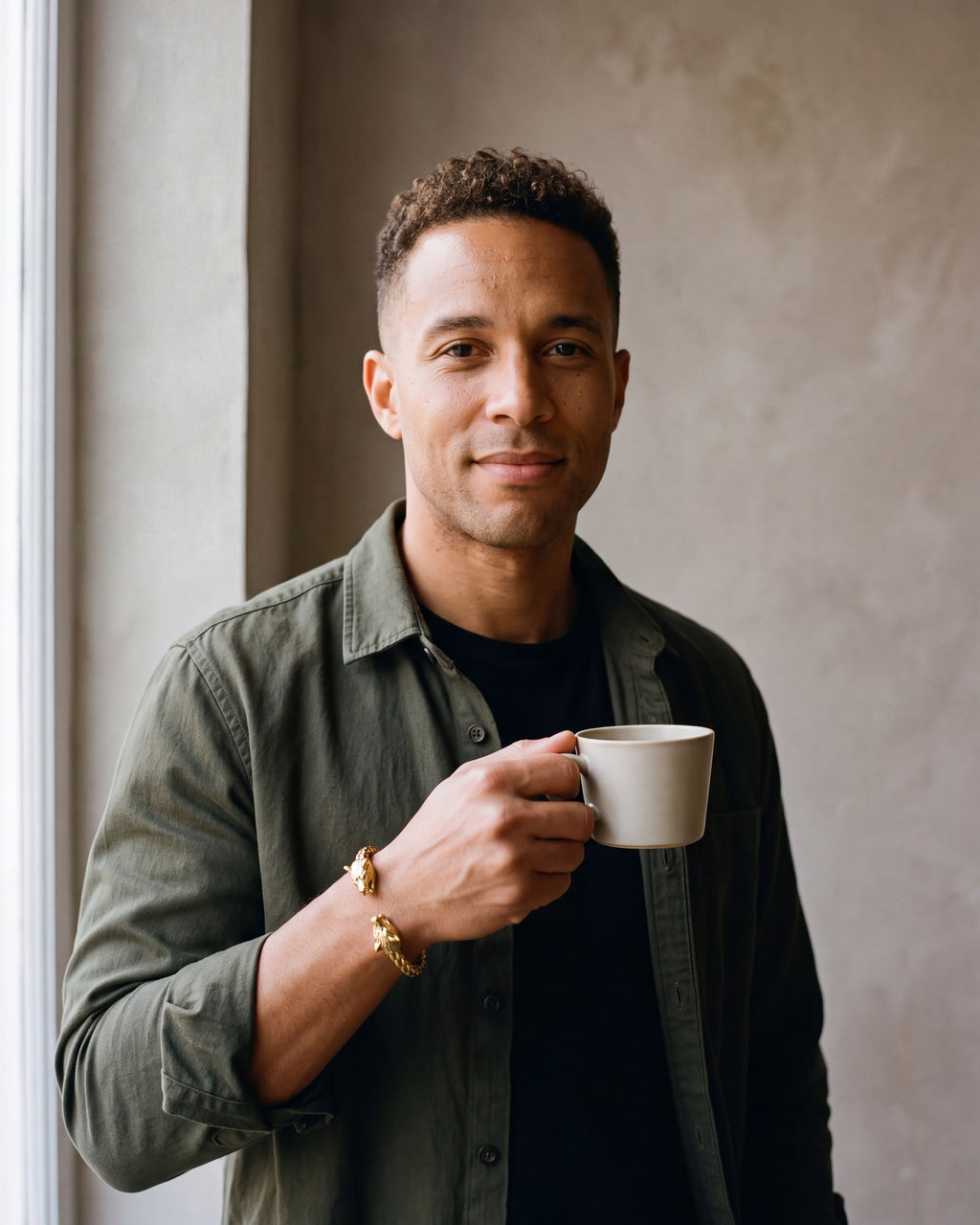 Second man in a dark olive overshirt open over a plain black t-shirt wearing the gold-tone Atlas wolf head braided cuff bracelet
