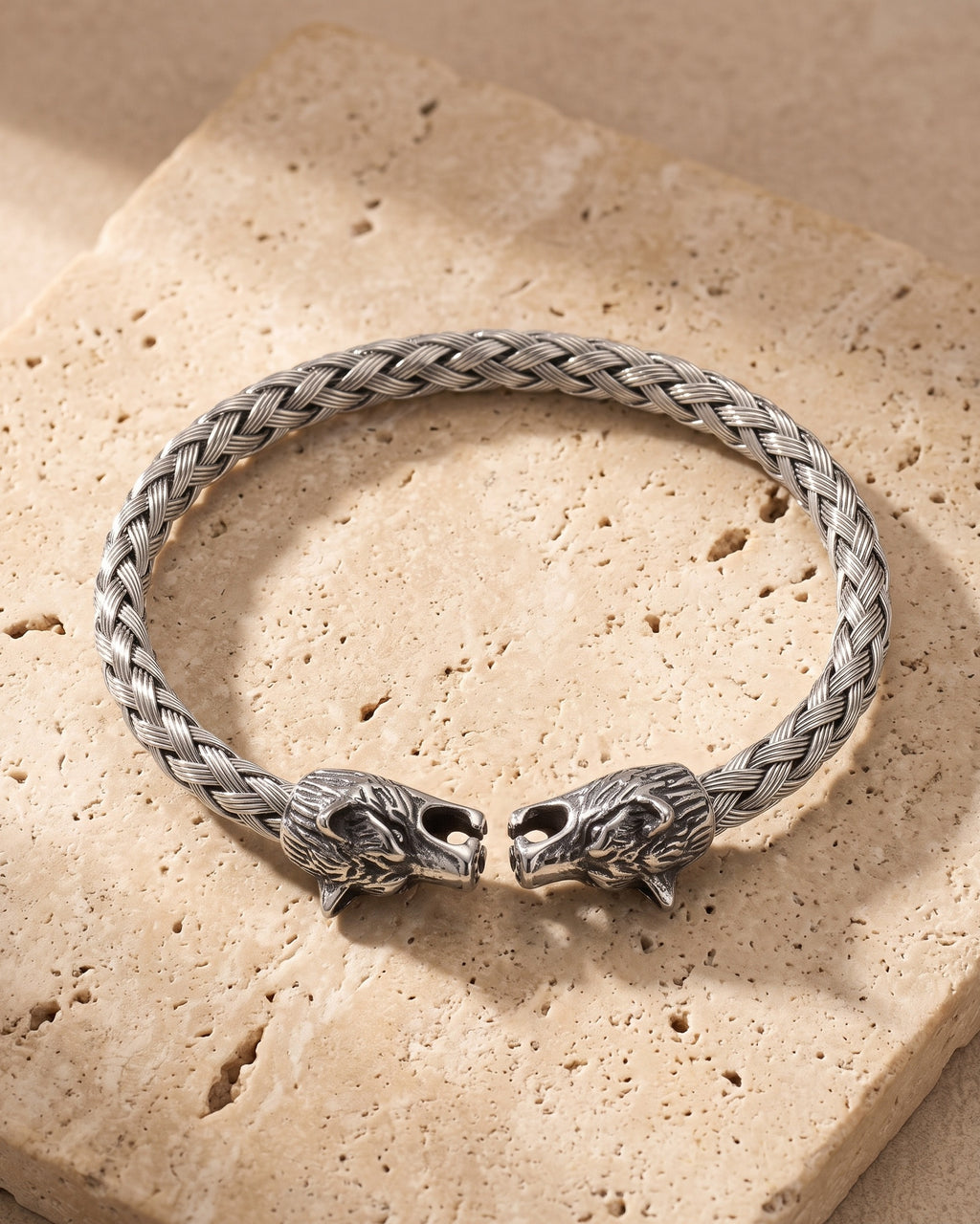 The whole silver-tone Atlas wolf head braided cuff bracelet lying on warm travertine stone