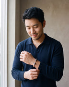 Man in a navy fine-gauge knit polo with an open collar by a window wearing the silver-tone Atlas wolf head braided cuff bracelet