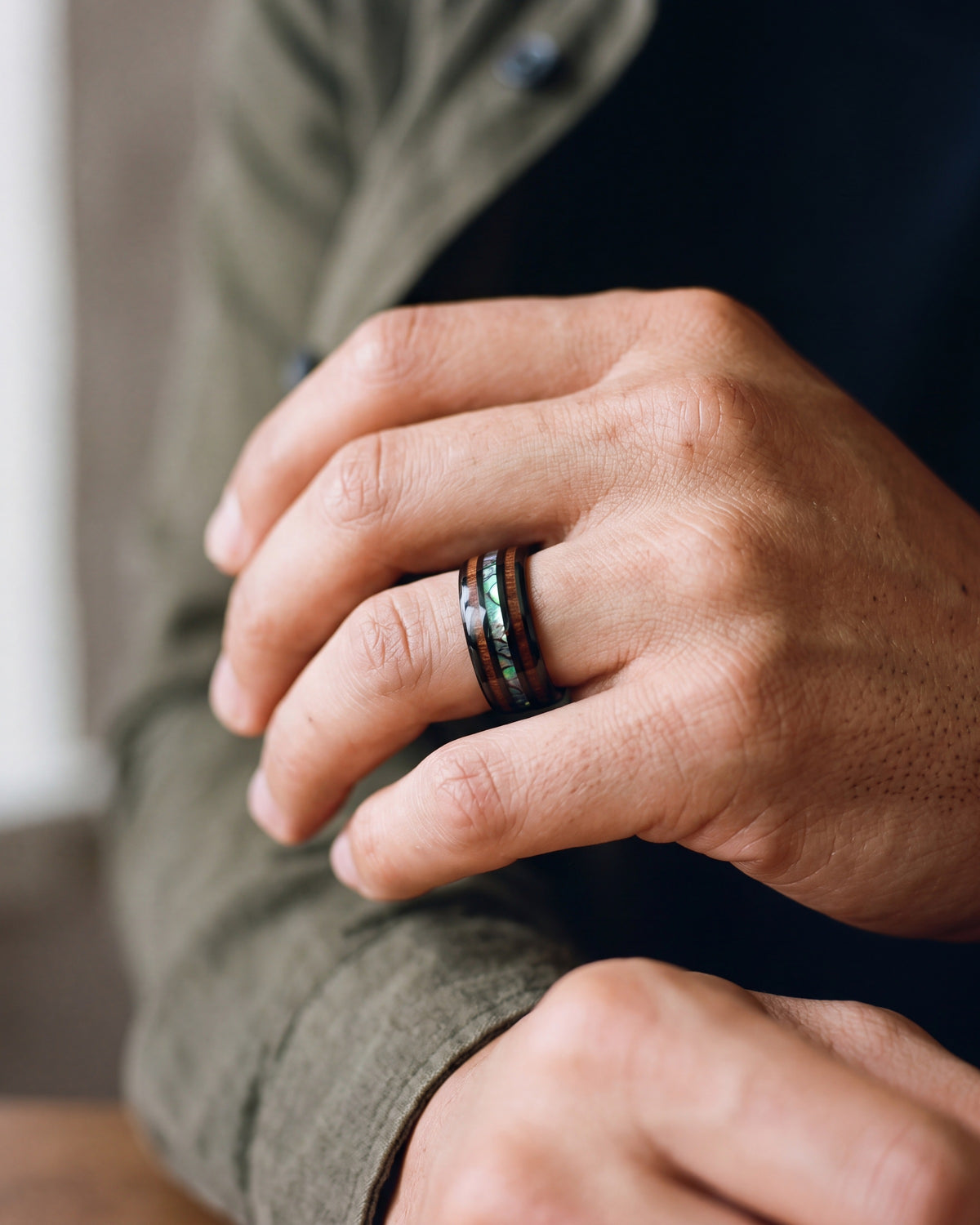 Close-up of the black Atlas wood and abalone band in black tungsten worn by a man, shown at true size