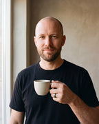 Man in a heavyweight black t-shirt by a window wearing the Atlas wood and meteorite-look inlay tungsten ring in silver-tone steel