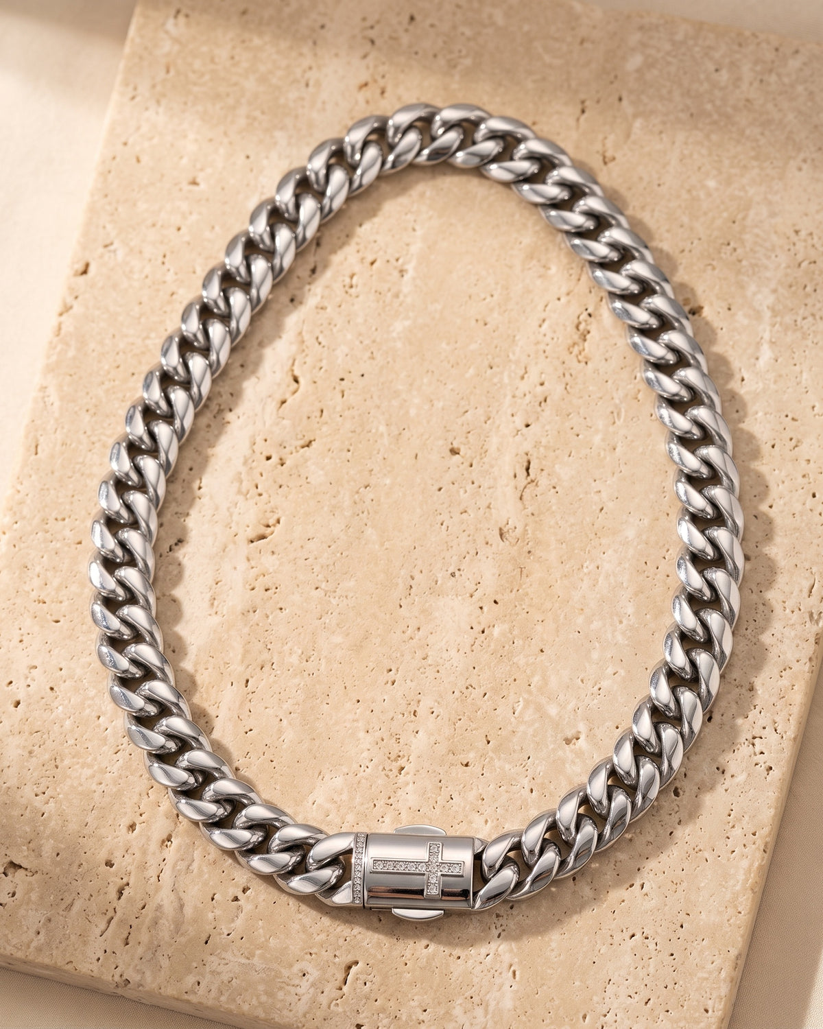 Entire Atlas Cuban chain with zircon cross clasp in silver-tone steel, lying flat on warm stone