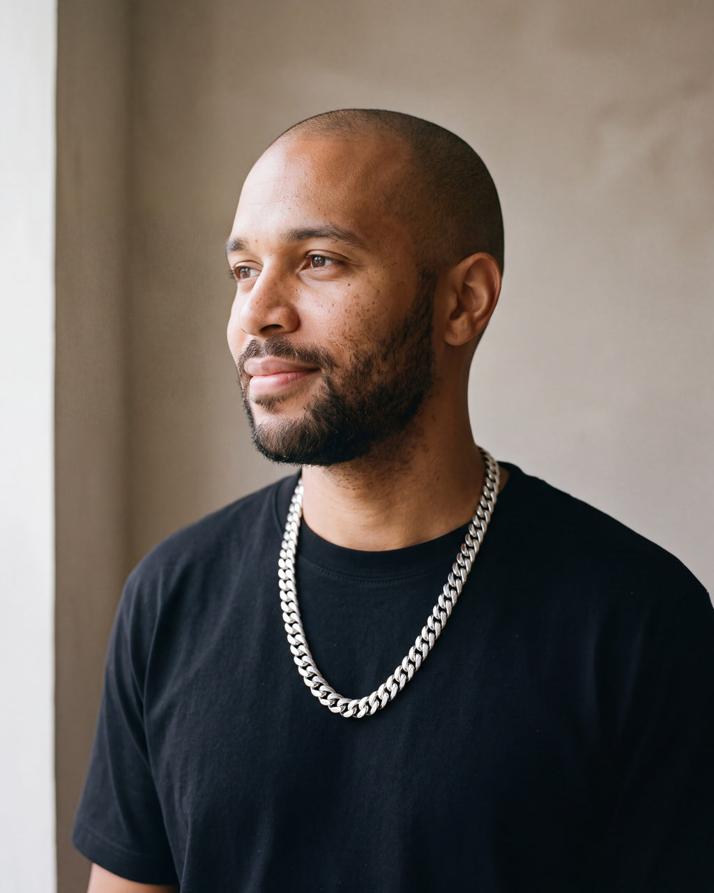 Man in a black t-shirt by a window wearing the Atlas Cuban chain with zircon cross clasp in silver-tone steel