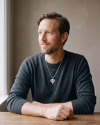 Man in a charcoal fine-gauge knit crew-neck sweater by a window wearing the silver-tone Atlas Egyptian Scarab Eye of Horus Pendant Necklace