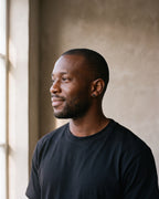 Man in a heavyweight black cotton crew-neck t-shirt by a window wearing the silver Atlas Black Disc Stud Earrings