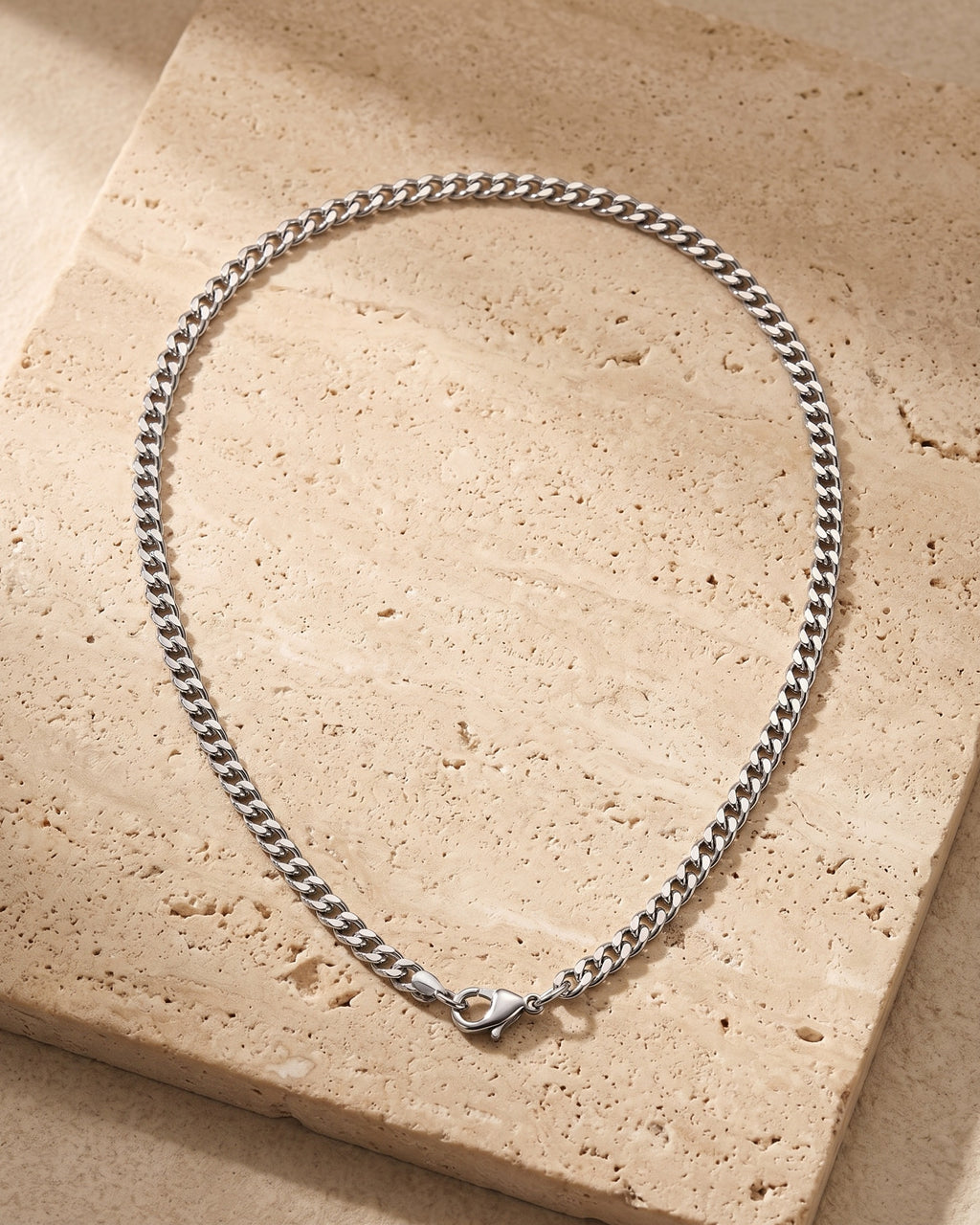 Silver Atlas 3 mm Cuban chain laid whole on warm stone, lobster clasp closed
