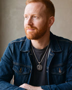 Man in a denim jacket seated at a table, wearing the Atlas Tree of Life pendant