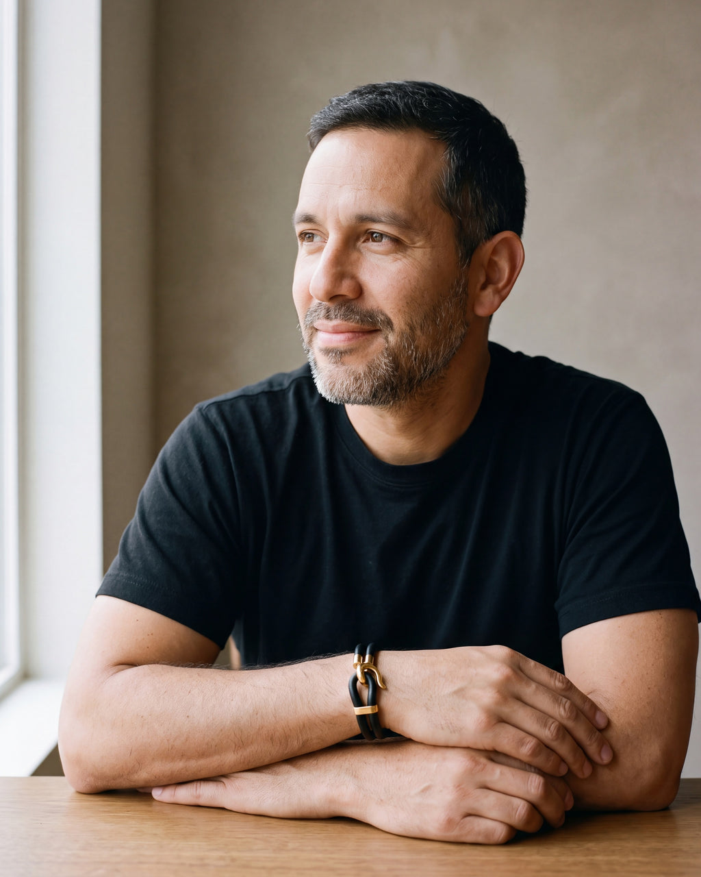 Man in a black T-shirt seated at a wooden table, wearing the smooth leather Atlas two-strand hook bracelet with gold-tone hook [c:smoothgoldtone]