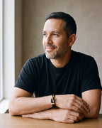Man in a black T-shirt seated at a wooden table, wearing the smooth leather Atlas two-strand hook bracelet with gold-tone hook [c:smoothgoldtone]