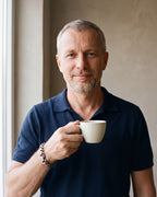 Man in a navy knit polo holding a coffee cup, wearing the silver Atlas dragon scale bracelet